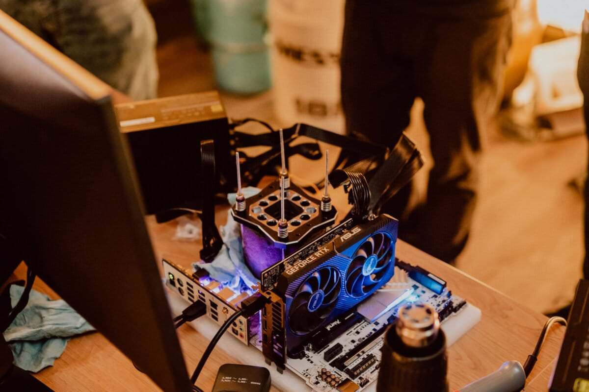   An open computer setup with a powerful graphics card and cooling system installed on the motherboard. The setup sits on a desk with various components and tools around it, apparently in the testing or building phase, probably as part of Marcin Krokowski's photo coverage of events. 