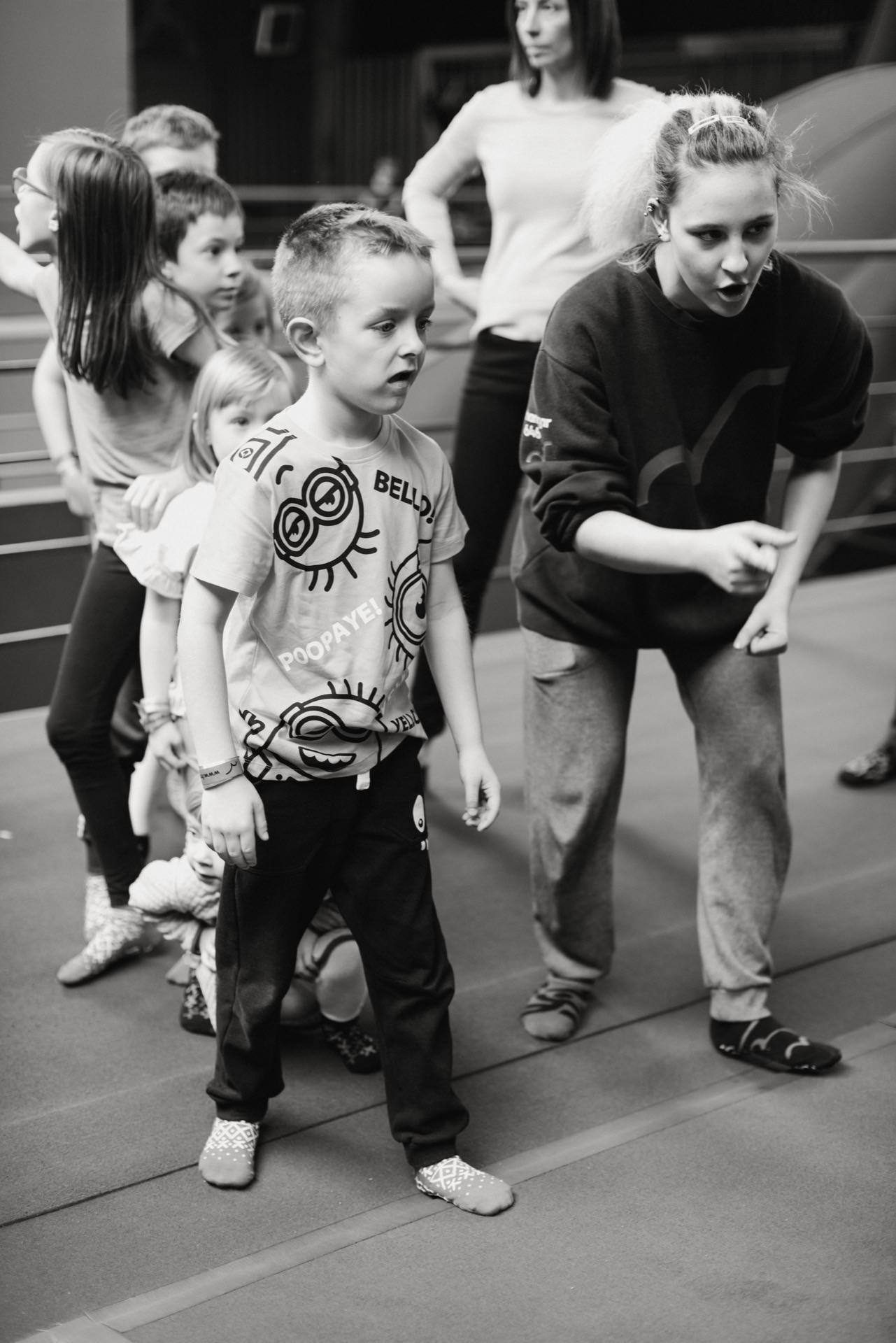 A group of children are waiting in line, and a woman in a sweatshirt and pants standing next to her is talking to the boy in front. This vibrant scene in the room was captured as part of event photography by event photographer Warsaw, perfectly documenting the energetic atmosphere. 