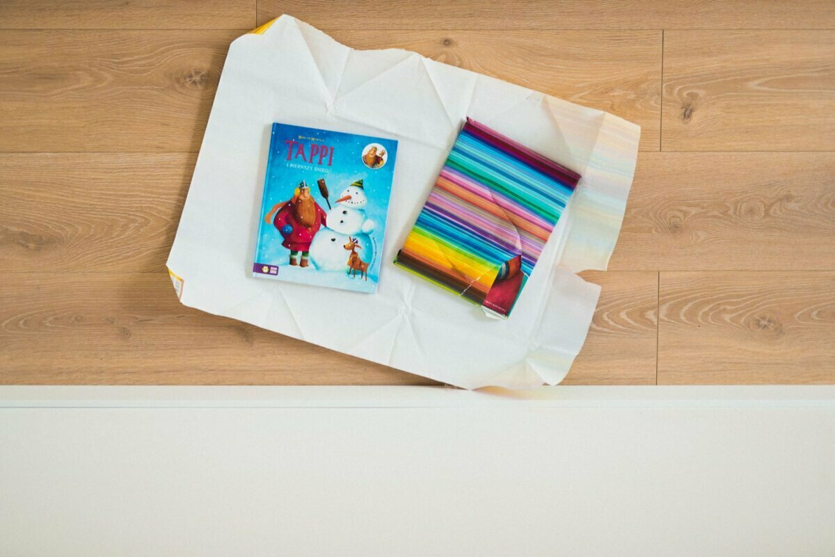 A DVD of an animated film depicting a snowman and a reindeer lies on top of partially open wrapping paper. Next to it are several colorful rolls of gift-wrapping paper, reminiscent of joyful moments captured in event photography. The items lie on a wooden floor.  