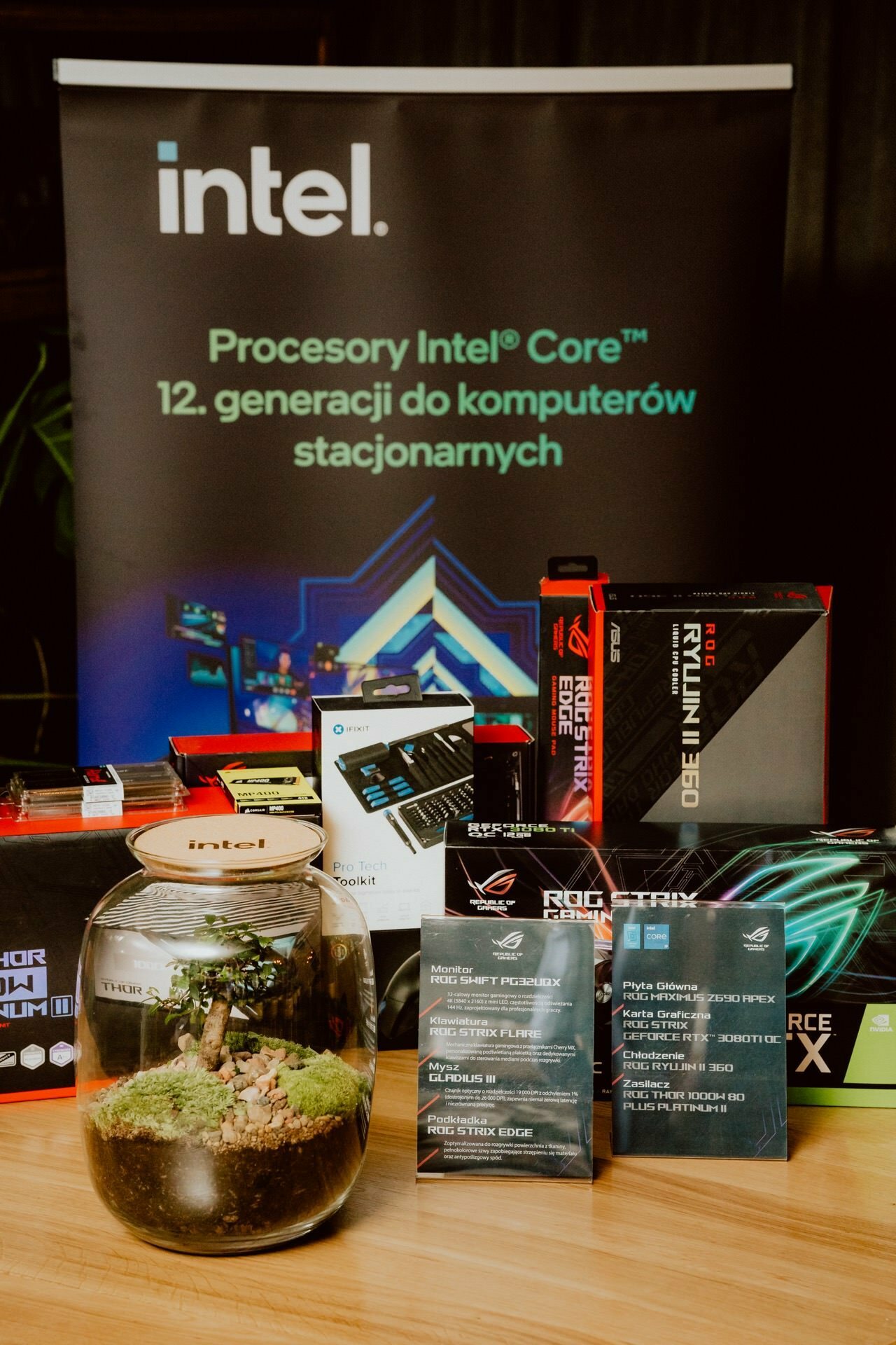 A display table at the press briefing shows various computer hardware components and accessories, including boxed Intel processors and ASUS ROG graphics cards. Behind the table, a banner with Intel's logo promoting Intel's 12th-generation Core desktop processors.  