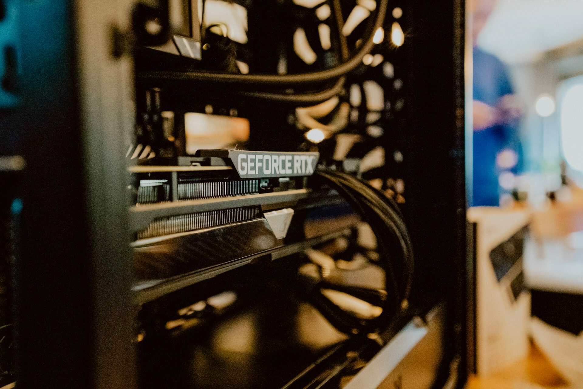 A close-up of an open computer case showing installed components, including a visible NVIDIA GeForce RTX graphics card. In the background, blurry images suggest a press briefing with a person standing next to other hardware. 