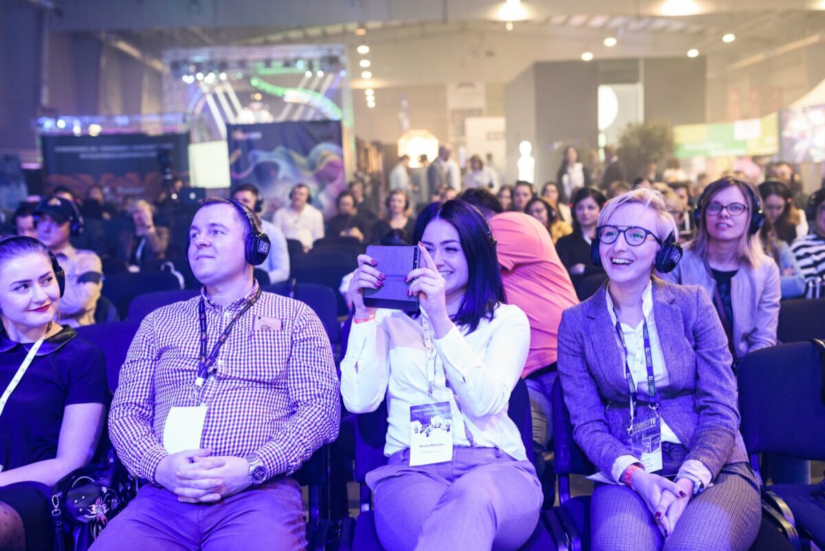 Smiling people in the audience and a woman taking pictures with her phone