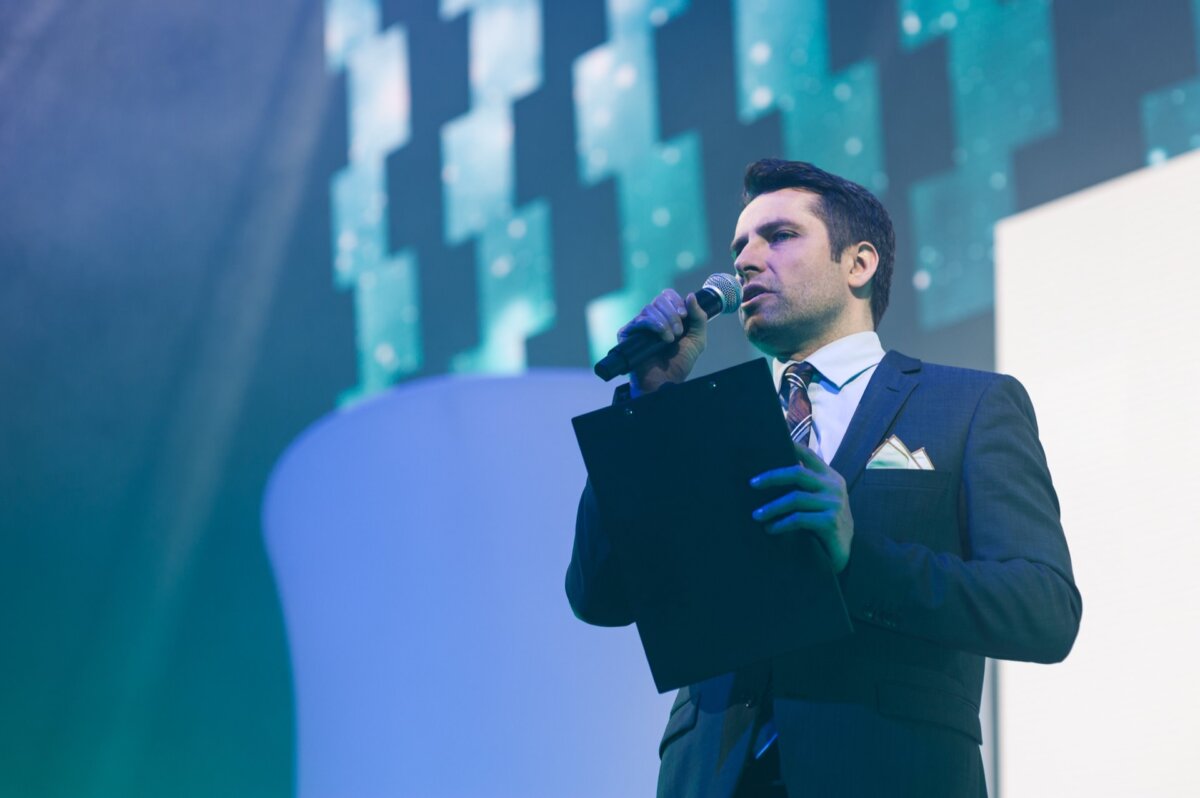 The presenter speaks on stage into a microphone