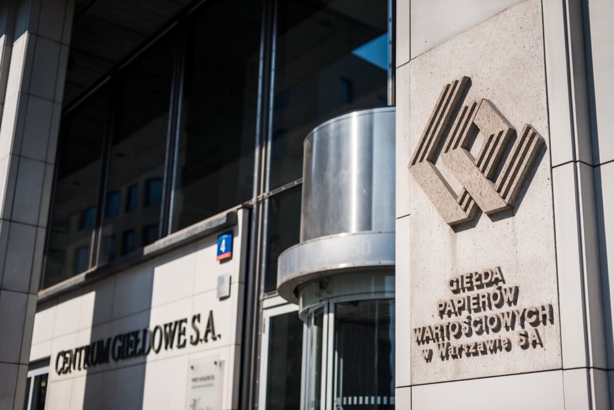 Das Äußere eines modernen Gebäudes mit den Worten 'Warsaw Stock Exchange SA' und 'Stock Exchange Centre SA' an der Wand neben der gläsernen Drehtür. Es sticht mit seiner polierten Steinfassade und dem Logo-Relief hervor und eignet sich ideal für Eventfotografie oder Fotoreportagen von Veranstaltungen.