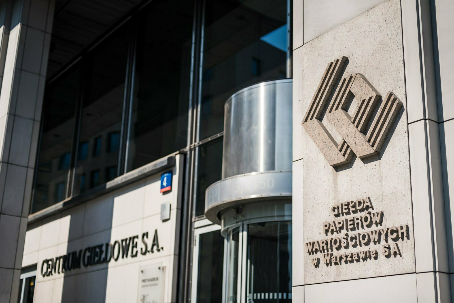 The exterior of a modern building with the words "Warsaw Stock Exchange SA" and "Stock Exchange Center SA" on the wall next to the glass revolving door. It stands out with its polished stone facade and logo relief, ideal for event photography or photo coverage of events. 