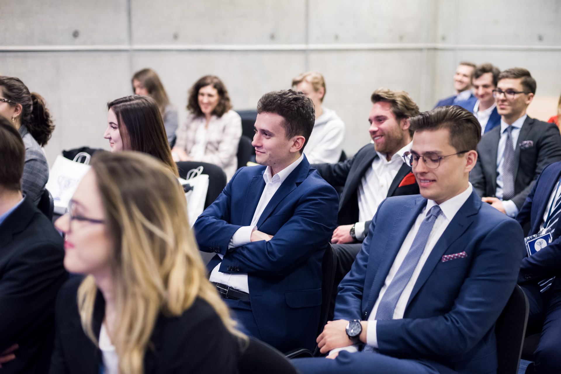 A group of people in formal attire sit in rows and listen attentively to a presentation or speaker. They look engaged, and some are smiling. The setting suggests a professional or educational event taking place in a modern, well-lit room, ideal for event photography by event photographer Warsaw.  