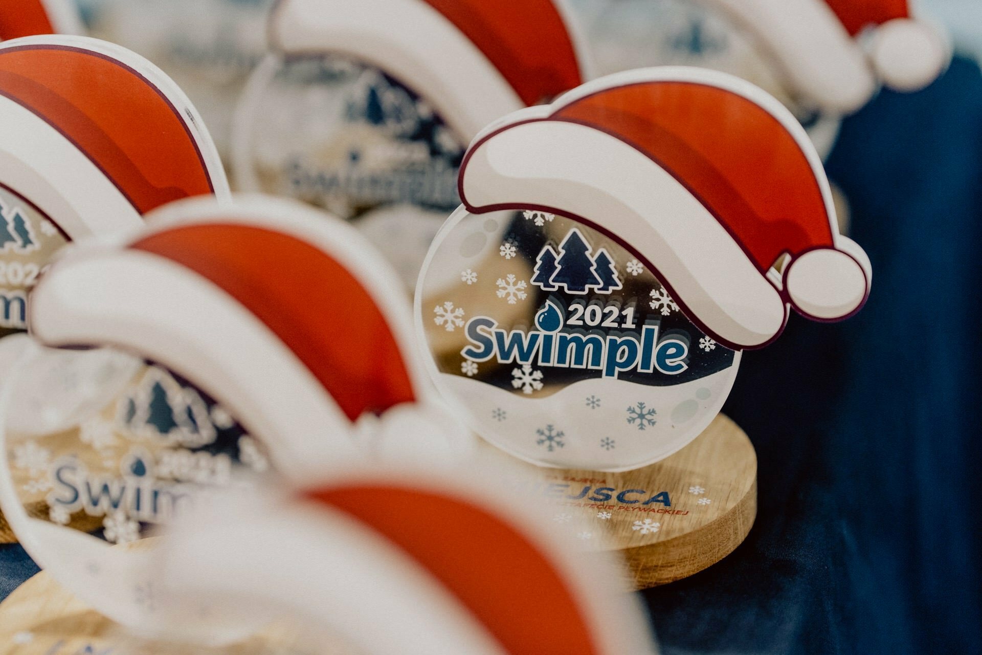 Rows of Christmas-themed prizes with the words "2021 Swimple" and a red Santa hat. The round-shaped awards with a snowflake background are mounted on a wooden base. These festive moments captured by Marcin Krokowski highlight his expertise as an event photographer in Warsaw.  