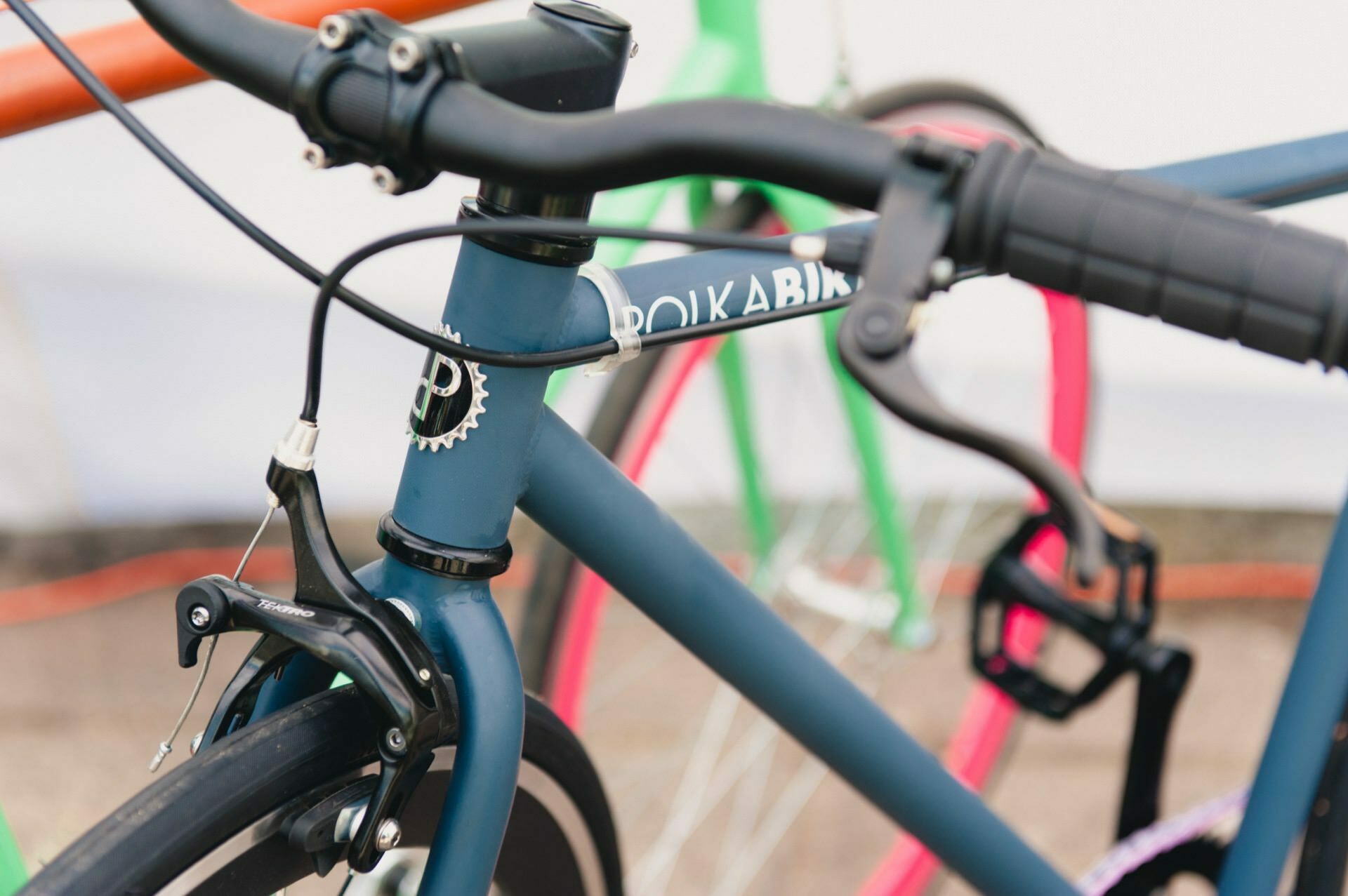 A close-up of the front of a parked blue bike with the "Doika Bike" branding on the frame. Captured by an event photographer, the focus is on the handlebars, brake lever and front brake, and parts of other bikes are visible in the background - as seen in the photo report from the fair. 