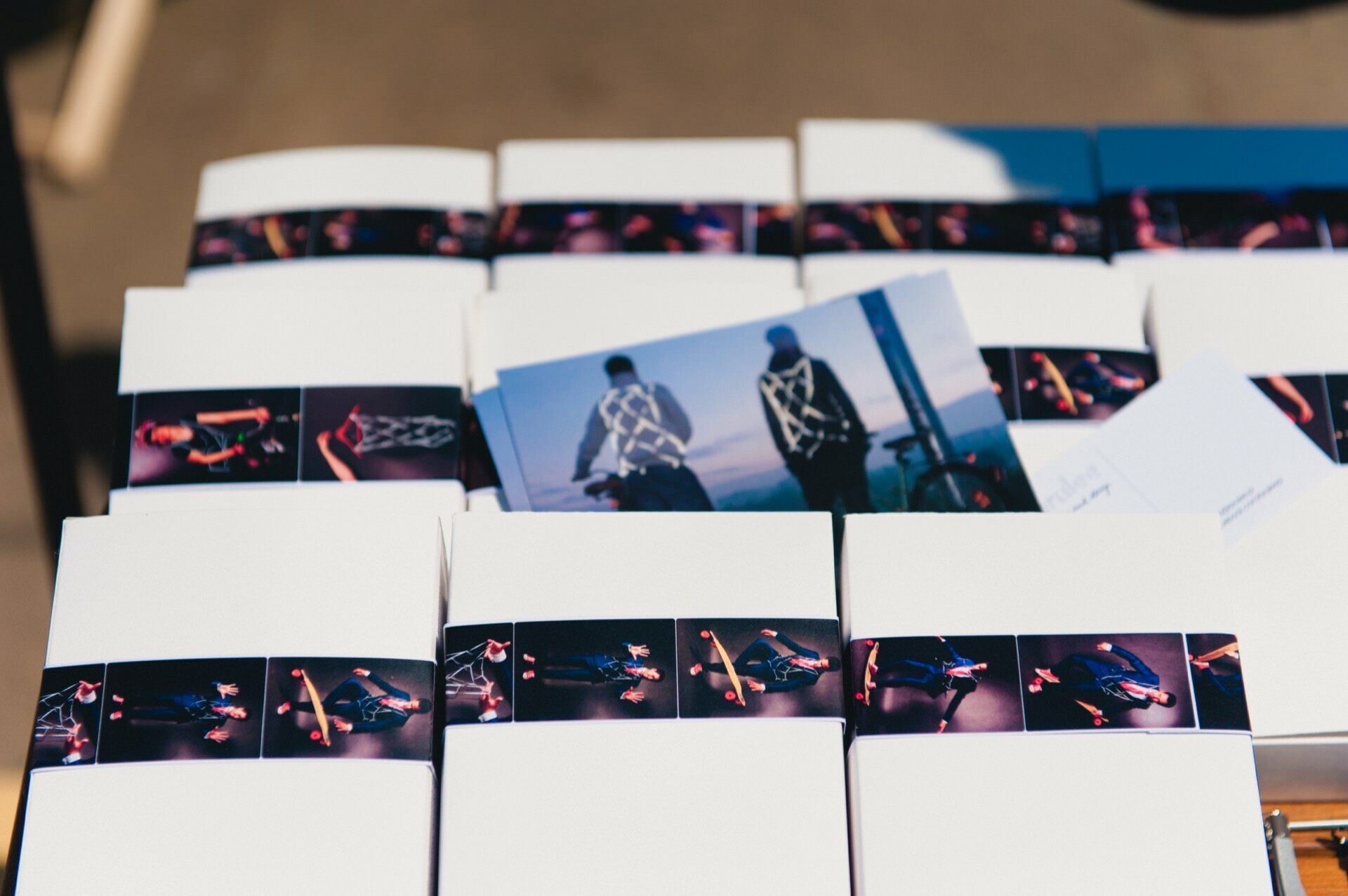 Rows of white gift boxes are arranged, each wrapped in a black band with photos of people wearing reflective items. On top of the boxes hangs a postcard with an image of two people wearing reflective vests, showing a photo essay of the fair by our talented event photographer. 