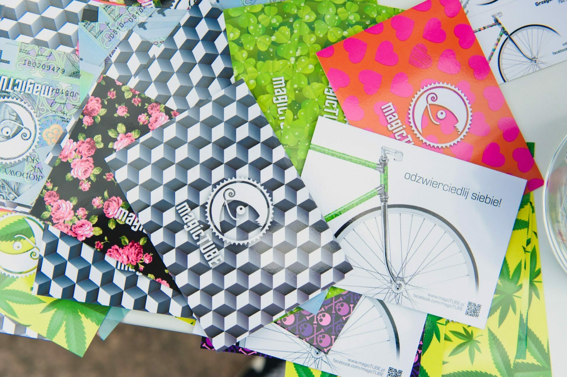 A variety of colorful flyers with different designs and patterns were spread out on the table. Some have geometric shapes, floral prints and leaf patterns, and one prominently features a bicycle. The text on one of the flyers reads "reflect yourself!". Capture every detail like an expert event photographer.