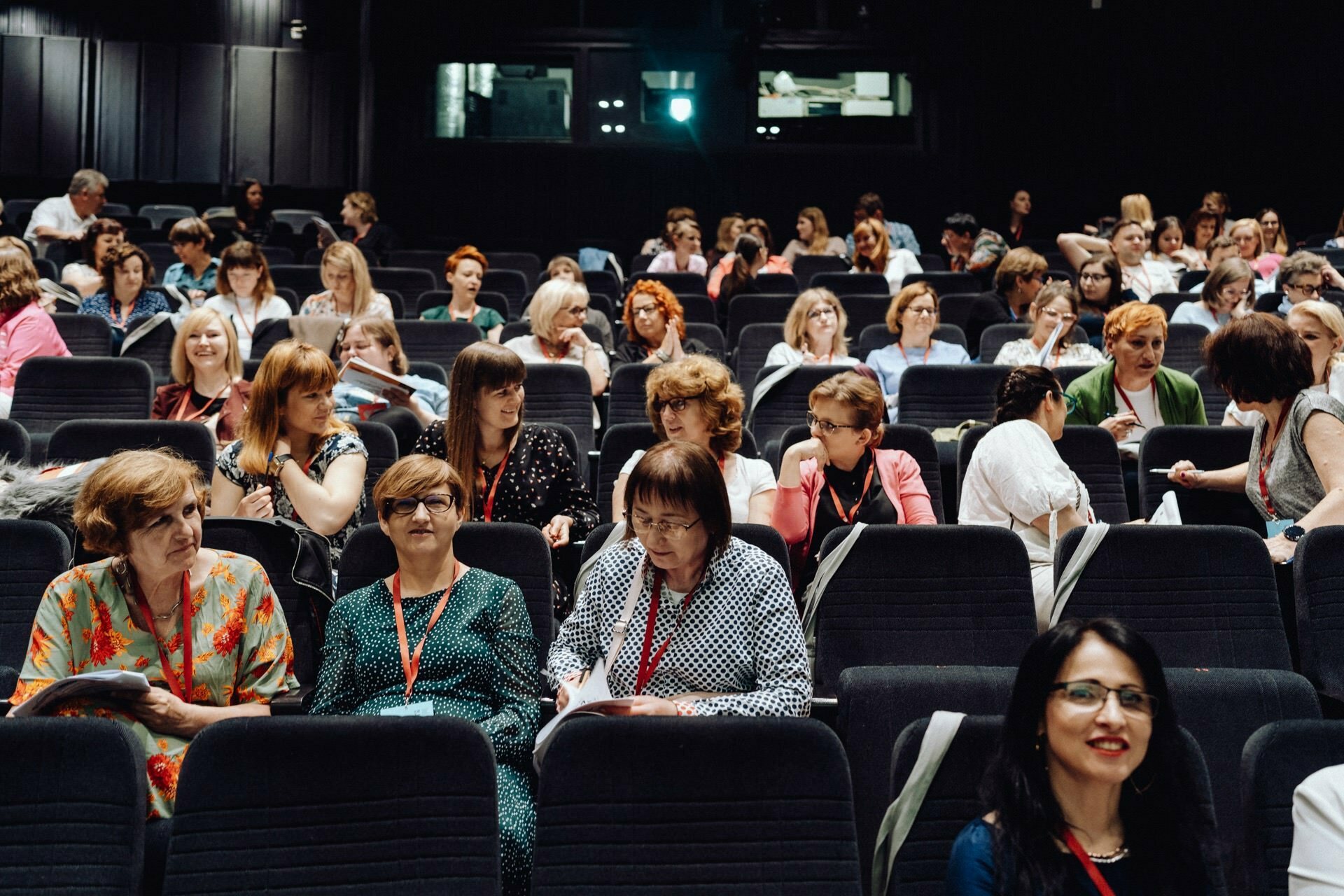 A diverse group of people seated in a large room, gaze intently ahead, capturing moments perfect for photo coverage of the event. Some people are engaged in conversation with each other. The setting suggests a conference or lecture, perfect for any photographic event.  