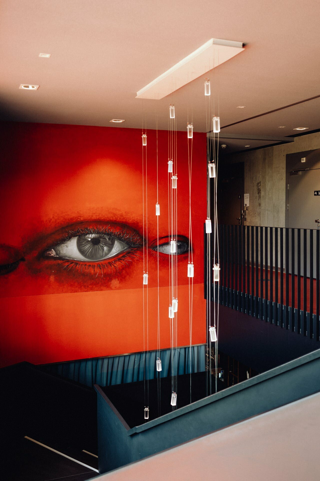 The modern interior is decorated with a large, vibrant mural depicting one eye on a red background. Suspended from the ceiling are numerous translucent light fixtures hanging at various lengths above a staircase with sleek black balustrades. The overall design is modern and striking - perfect for any Warsaw photographer to capture.  