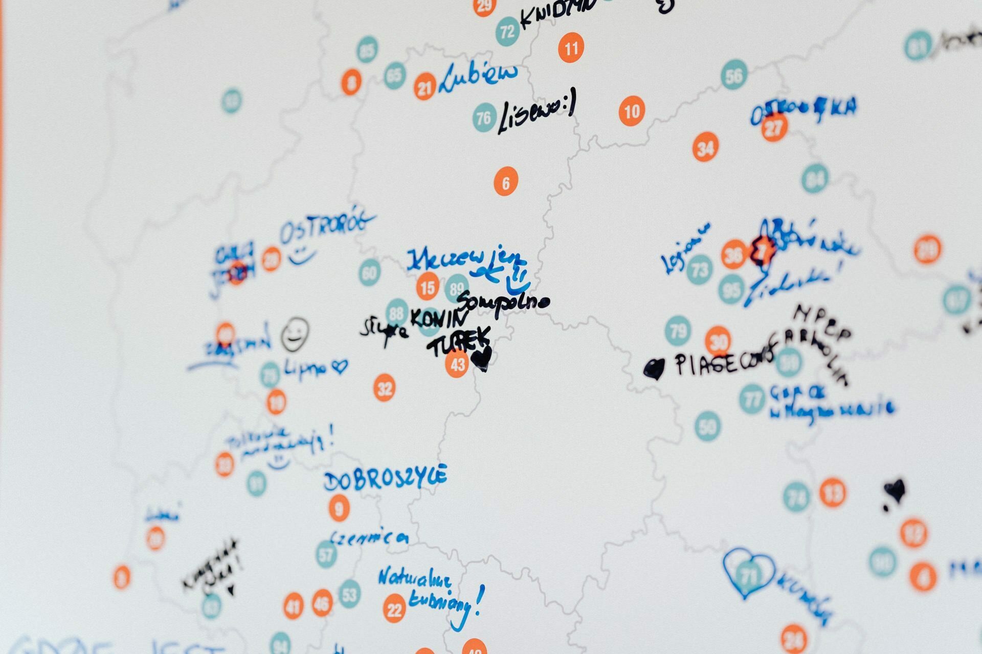 A white map with numerous hand-drawn notes, scribbles and symbols in various colored markers, reminiscent of an *event photo*. The map includes numbers in a circle, locations marked with stars, hearts and other drawings, as well as text written in blue, black and orange ink. 