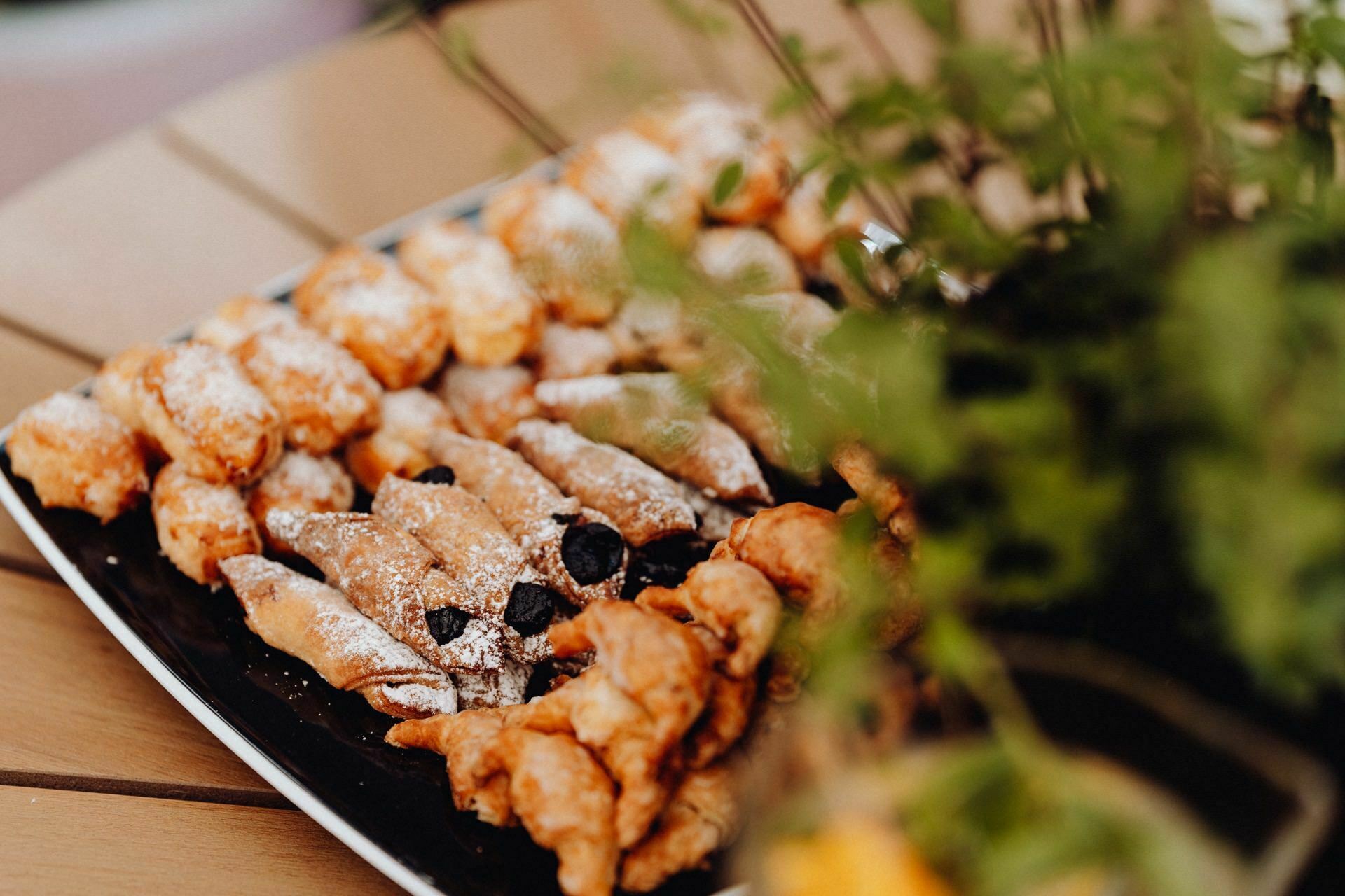 A plate of assorted cookies sprinkled with powdered sugar, some sprinkled with berries. The plate is set on a wooden table captured in a photo essay of the event, with a blurry background of green leaves on the right side of the photo. 