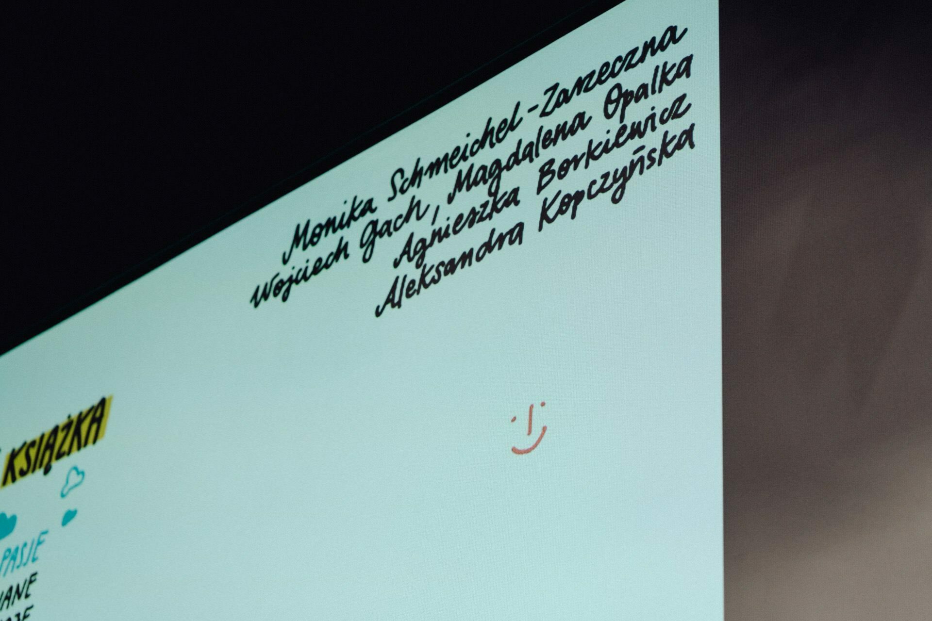 On the plaque is a list of names handwritten in black ink, including Monica Schmeichel-Zarzeczna, Wojciech Gach, Agnieszka Borek and Aleksandra Korczynska. Next to it is a small, simple drawing depicting a smiling face. This scene captures the memories of our photo report from the event.   