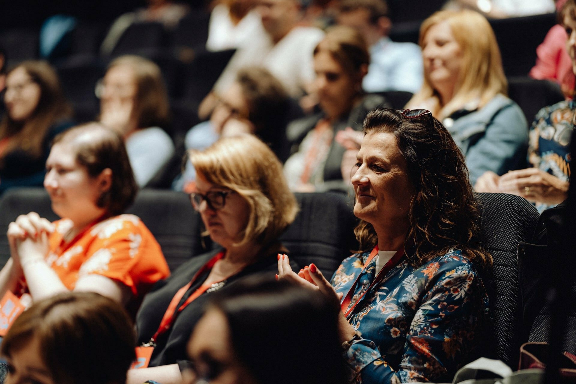 A diverse group of people sit in the auditorium and listen attentively to the presentation. The audience is of all ages and seems engaged, sometimes clapping. This photo report of the event perfectly captures the atmosphere, suggesting a well-organized conference or seminar.  