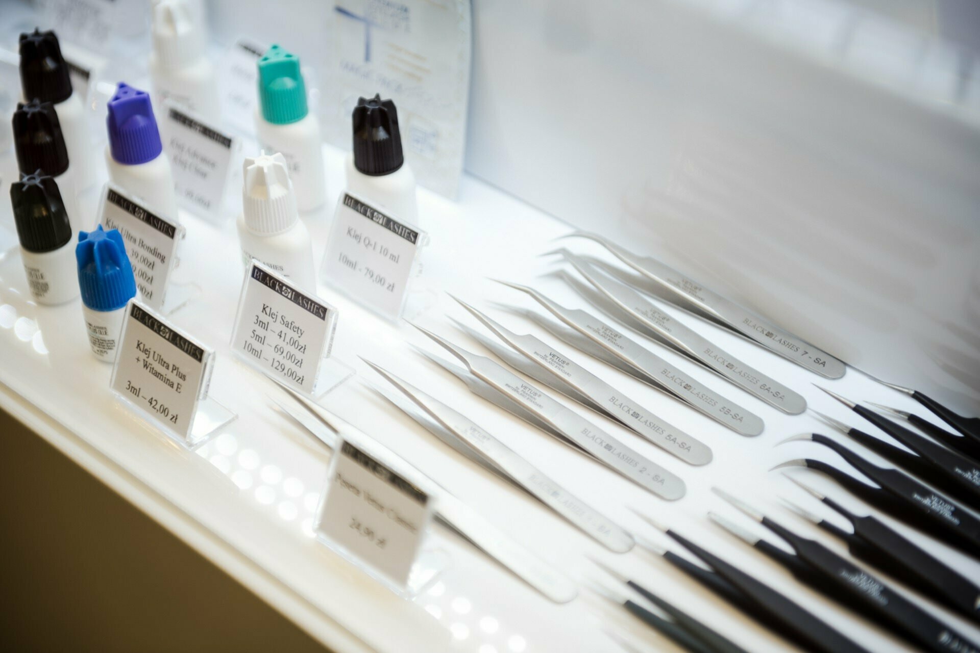 The display case containing various precision tools and bottles is impeccably organized. On the right are neatly arranged tweezers of various shapes and sizes, and on the left are small bottles with colorful caps. Also visible are cards with descriptions of each item, taken by Marcin Krokowski, a photographer in Warsaw.  