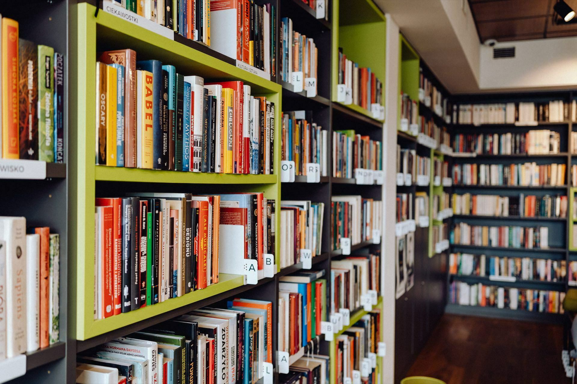 Picture a well-organized library with many shelves filled with a variety of books. The books are arranged by alphabetically labeled chapters. Bright lighting and a cozy atmosphere encourage visitors to explore the extensive collection, as does a detailed photo essay of the event curated by a talented photographer from Warsaw.  