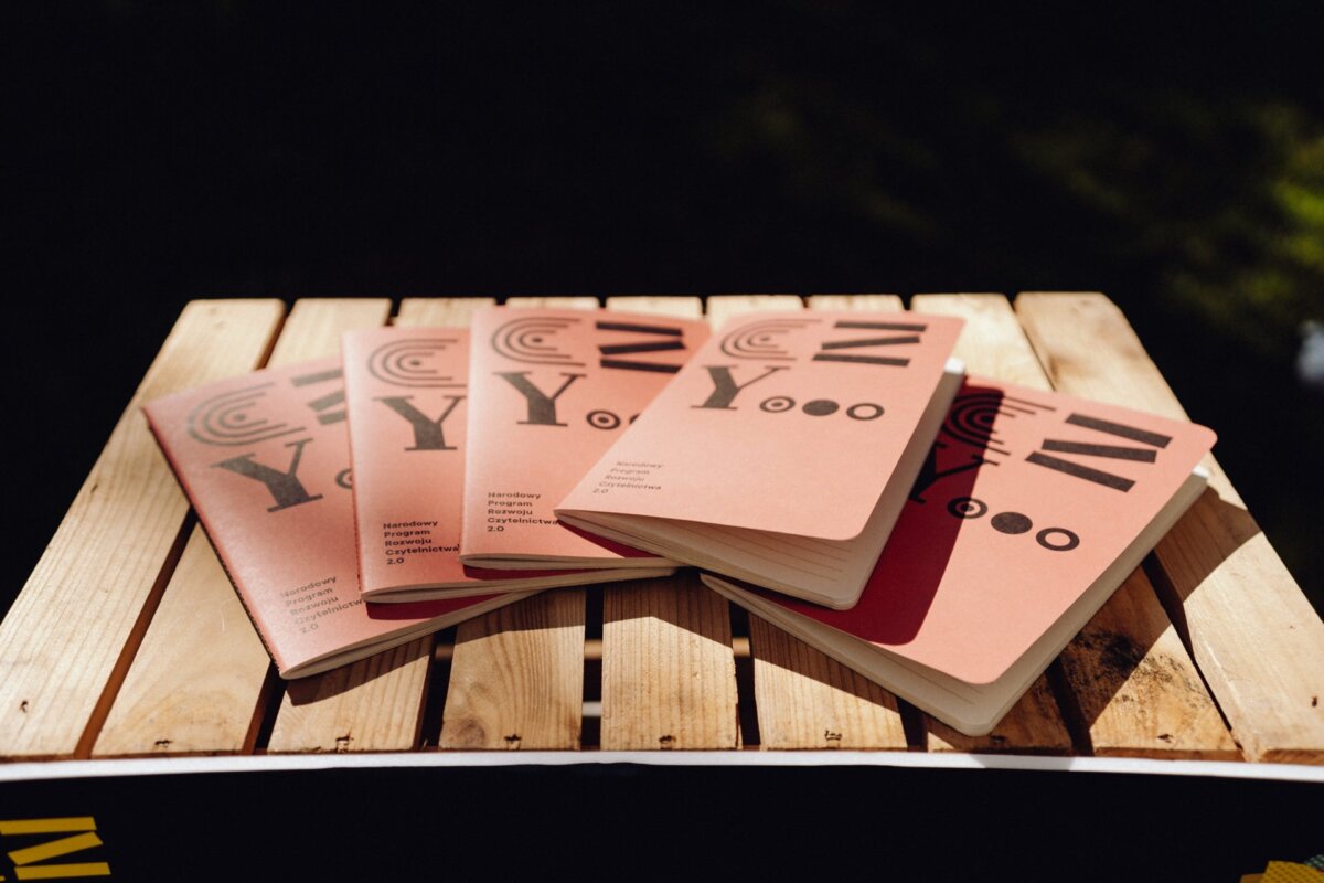 Several notebooks with brown covers with the letters "C Y" and circular designs are spread out on a wooden surface. The notebooks are arranged with their covers facing upward, depicting similar typography and design elements. Sunlight casts shadows on the surface, creating a scene that is beautifully captured by *event photographer Warsaw*.  