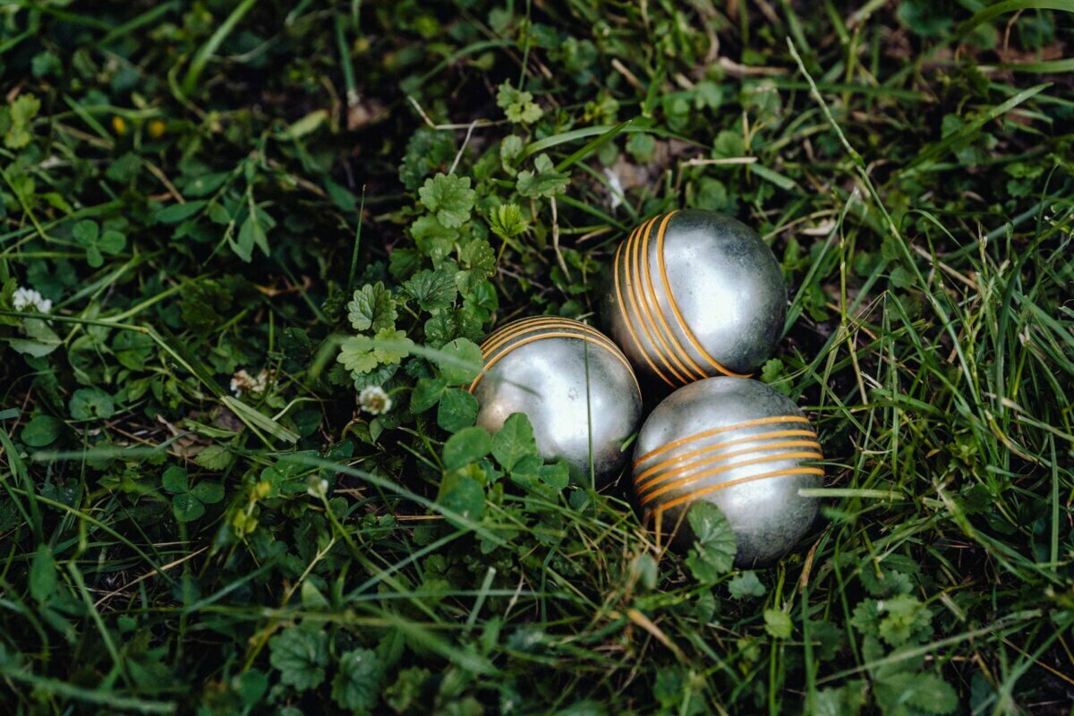 Three metal pétanque balls with orange stripes lie close together on the grass among green leaves, a perfect shot by a skilled Warsaw event photographer.