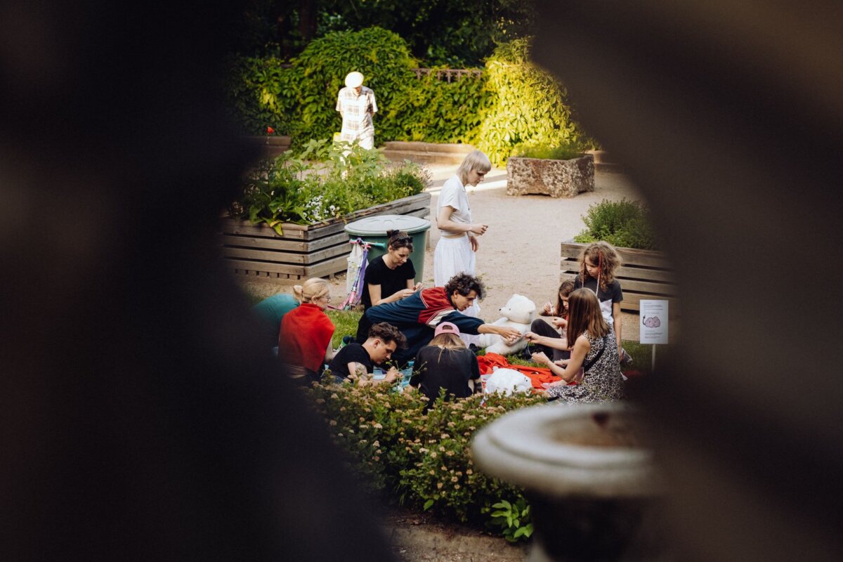 A group of people are sitting and standing around a raised garden bed in the park, doing various activities. They appear to be working together on a joint project. The surroundings are surrounded by lush greenery, and other people can be seen in the background, which was perfectly captured by a photographer from Warsaw for a photo report of the event.  