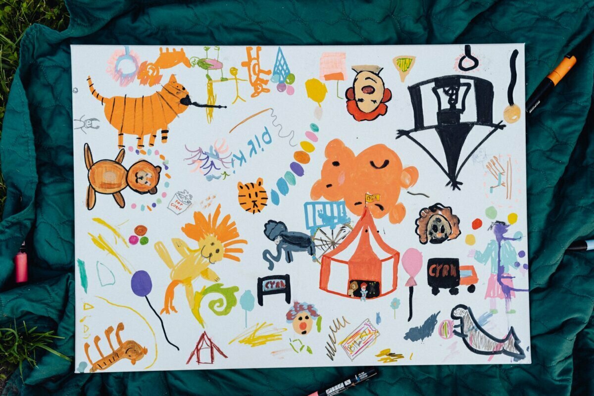 A colorful children's drawing on white canvas superimposed on green fabric, perfectly captured in our event photo report. The drawing depicts various animals, including a tiger, lion and owl, as well as fanciful shapes, flowers and a tent. Bright markers and scribbles fill the canvas.  