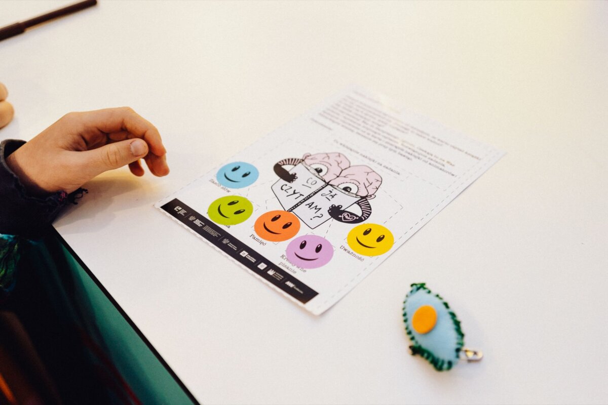 The hand rests on a table next to a worksheet with an illustration of a child saying "I can't say no." Below the illustration are five colorful smiling faces. Next to the worksheet lies an egg-shaped keychain that catches the eye like a photograph taken by a talented photographer from Warsaw.  