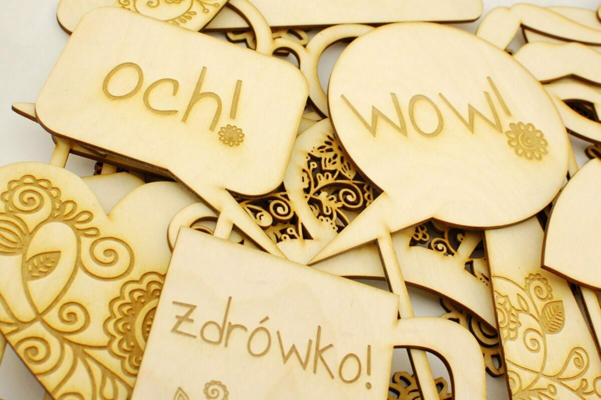 A collection of decorative wooden balloons and hearts with engravings, perfect for any event photographed by Marcin Krokowski. Some contain Polish words such as "och!" (oh!), "wow!" and "zdrowko!" (thanks!). Among the designs are intricate floral patterns.