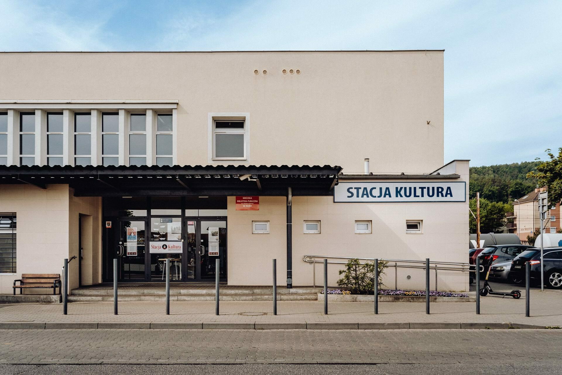 The photo shows a bright building with the sign "Culture Station" above the entrance. The structure has large windows and a canopy over the door. Several cars are parked to the right, and a small ramp leads to the entrance, providing a perfect setting for the photo event.  