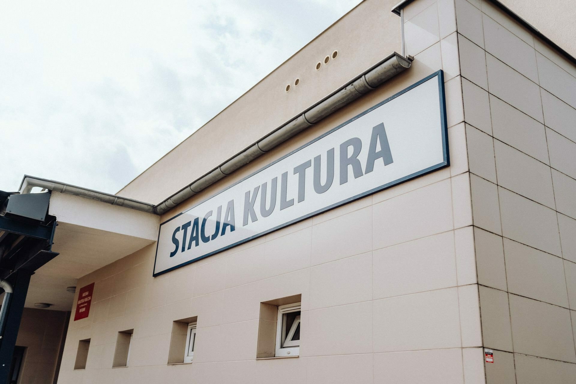 A modern beige building with the words "STATION OF CULTURE" exposed in large letters. The design incorporates small windows and a subtle overhang. The sky is overcast, which adds soft, diffused lighting to the scene - perfect for event photography by event photographer Warsaw.  