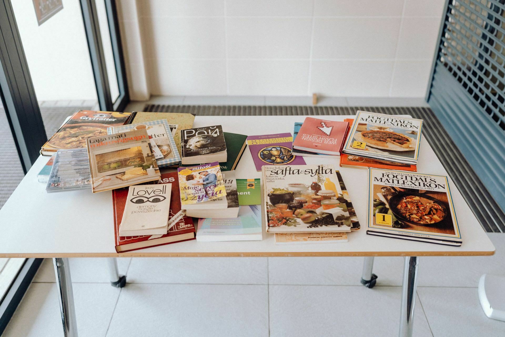 The table is set with an assortment of cookbooks and cooking magazines in various languages and designs. The books contain a variety of recipes, cooking techniques and food photographs, providing insight into different cuisines and cooking styles - as does a well-chosen photo essay of the event. 