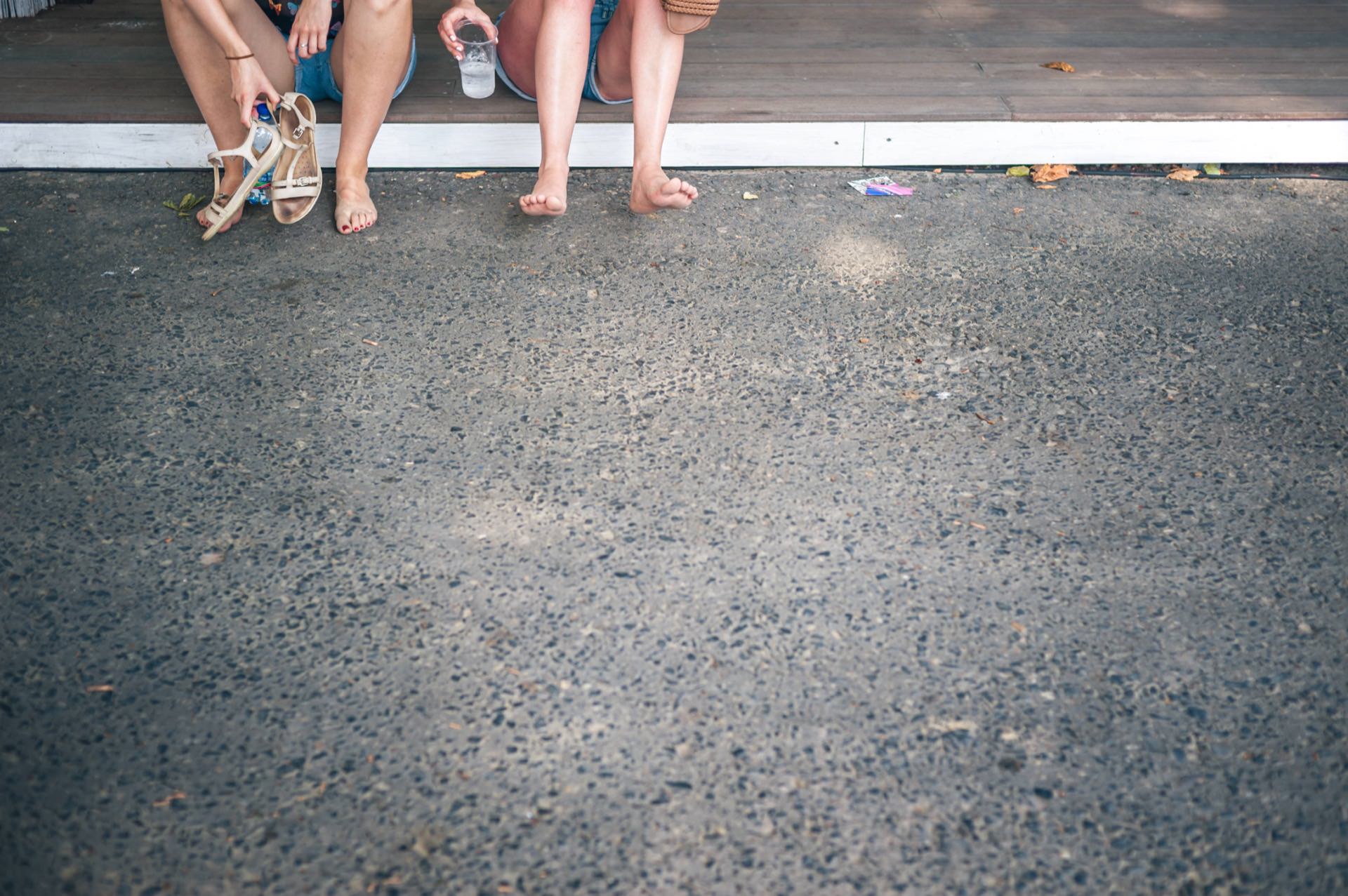 Three people sit on a step with their legs dangling, one wearing white sandals, another barefoot, and the third with one leg raised. They seem relaxed in this Photo Report from the fair, with the cobblestone area in the foreground and leaves scattered around. 