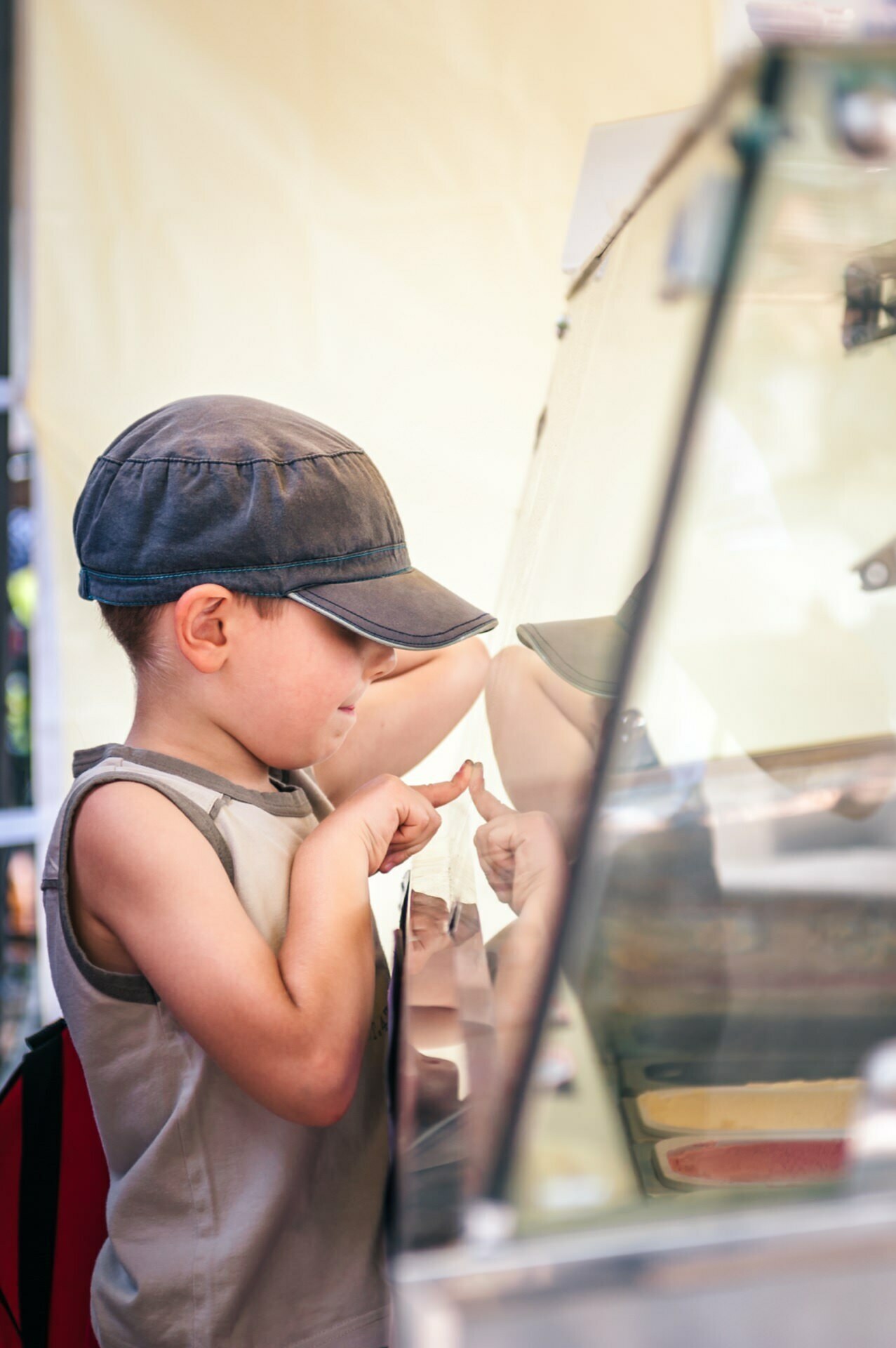 A young boy dressed in a sleeveless shirt and cap is carefully examining the items in the glass display case, pointing his finger at something. This photo could easily be part of a vibrant photo essay of the fair, capturing the vibrant essence of an outdoor market. 