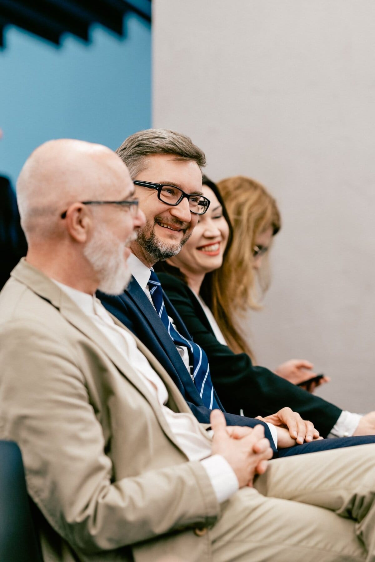 Four people are sitting next to each other at a party, smiling and having a pleasant conversation. The man on the left has a bald head and a white beard, while the two people in the middle wear glasses. This professional setting was perfectly captured by Marcin Krokowski, a talented event photographer in Warsaw.  