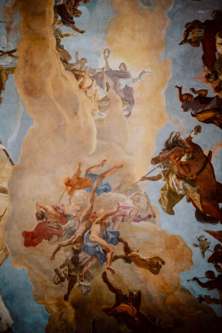 The ceiling is decorated with a detailed fresco depicting a dynamic scene of mythological figures and horses among clouds and sky. The figures are shown in dramatic poses, symbolizing movement and heavenly themes. The colors are rich and the composition is complex and vivid.  