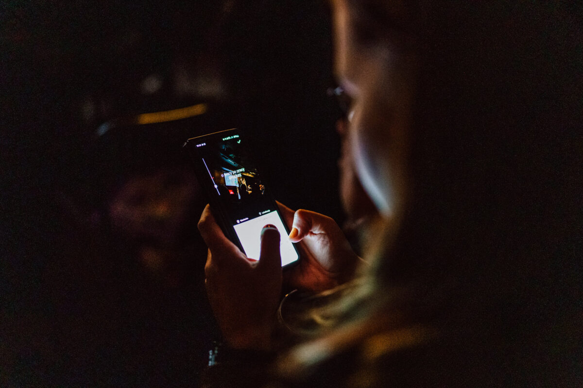 Nie mow do mnie ASAP Klub Komediowy 036 Eine Person hält in einer dunklen Umgebung ein Smartphone in der Hand, auf dessen hintergrundbeleuchtetem Bildschirm das gerade aufgenommene Foto zu sehen ist. Nur die Hände und ein Teil des Gesichts sind sichtbar, und die Hauptlichtquelle ist der Bildschirm des Telefons.