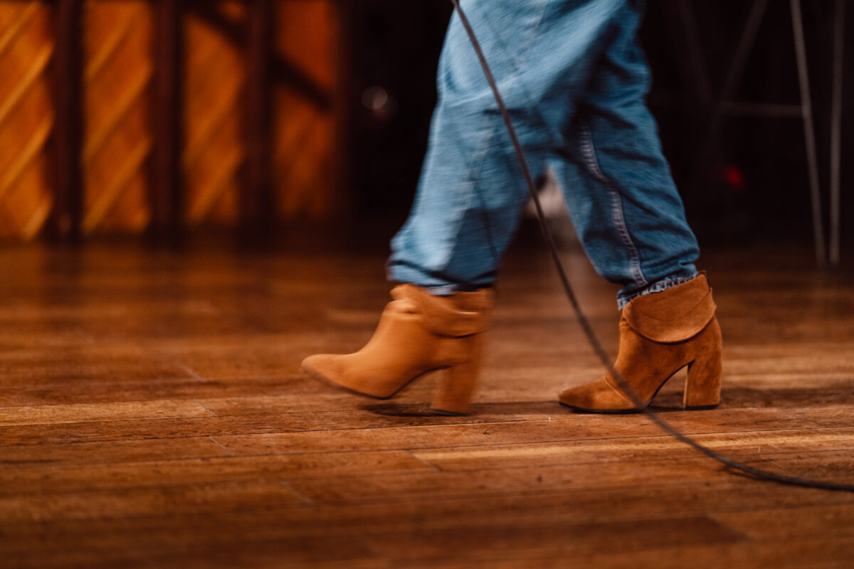 Nie mow do mnie ASAP Klub Komediowy 038 Eine Person in blauen Jeans und braunen Stöckelschuhen geht auf einem Holzboden, an dem ein schwarzes Kabel entlangläuft. Der Hintergrund ist sanft verschwommen.