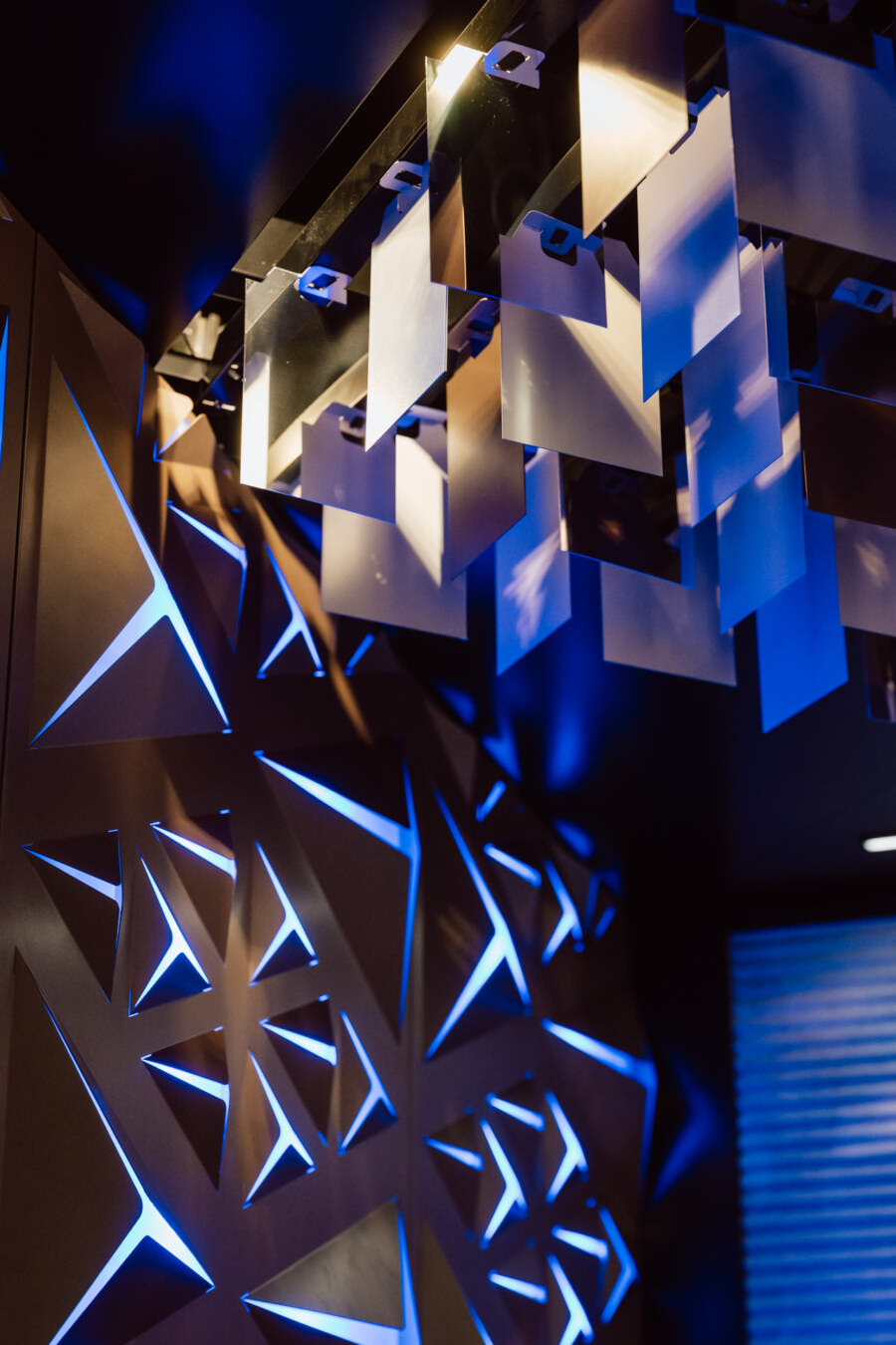 Geometrische Wandpaneele mit blauer LED-Beleuchtung und metallische, reflektierende Deckenplatten schaffen ein modernes, futuristisches Innendesign.