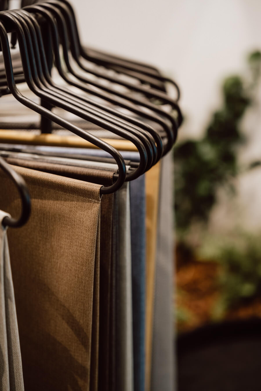Nahaufnahme von schwarzen Metallbügeln mit verschiedenen Stoffmustern in neutralen und gedeckten Farben wie Braun, Grau und Beige, mit einem unscharfen grünen Hintergrund.