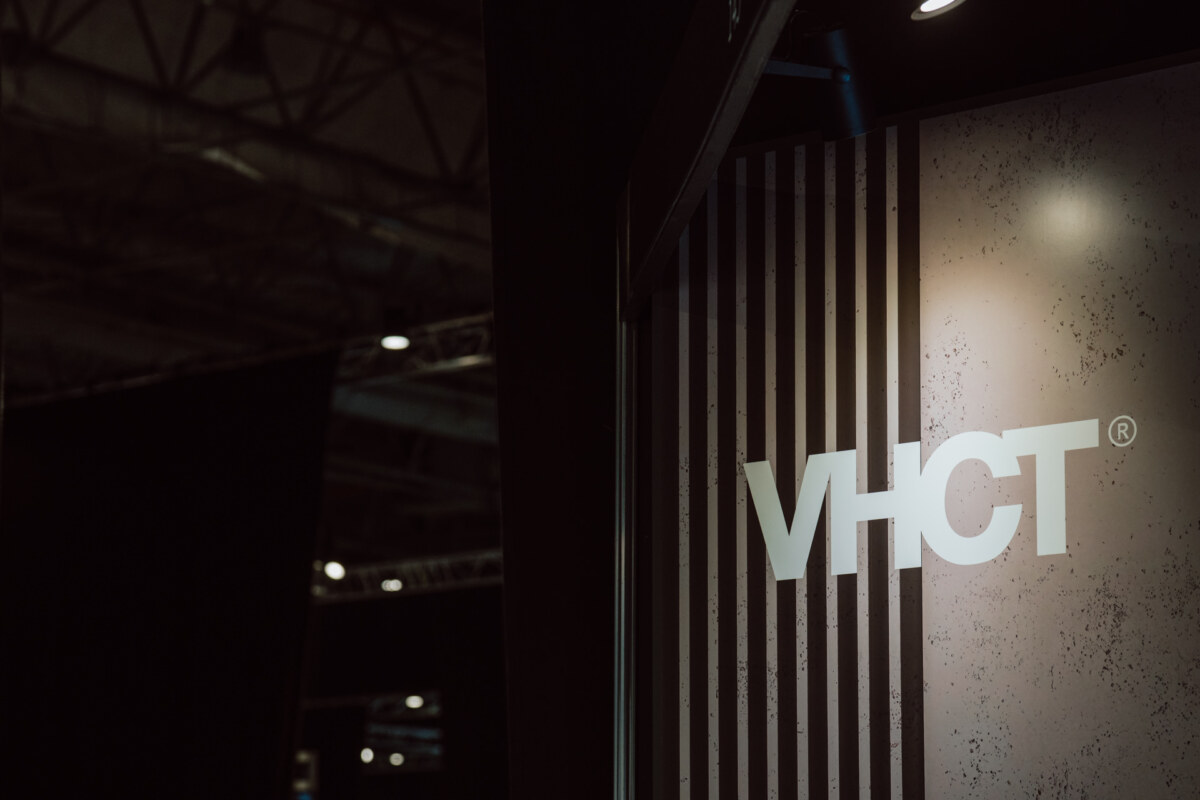 reportaz targi architektura architectatwork 2025 71 Nahaufnahme einer Wand mit vertikalen schwarzen und weißen Streifen, auf denen die weißen Buchstaben 'VHCT®' in einem schwach beleuchteten Innenraum leuchten.