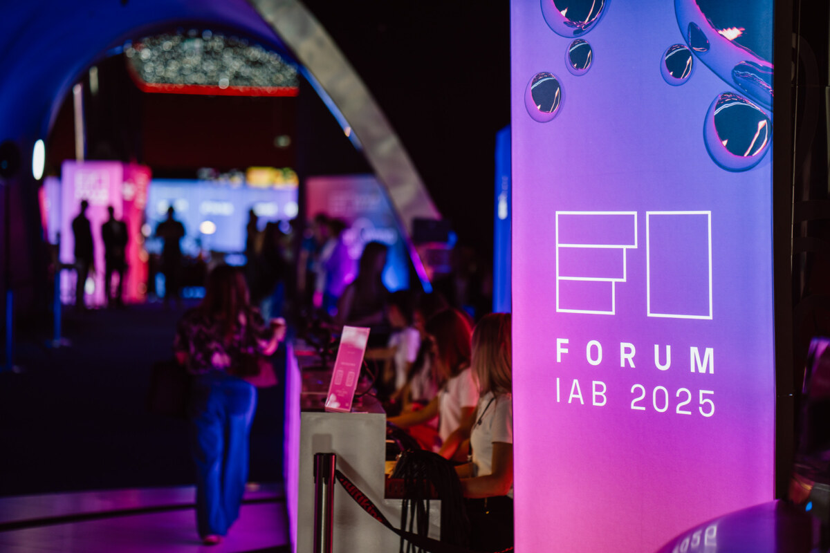 Jasno oświetlony napis "Forum IAB 2025" na wydarzeniu wewnątrz budynku, z zebranymi ludźmi i kolorowymi światłami tworzącymi żywą atmosferę w tle.