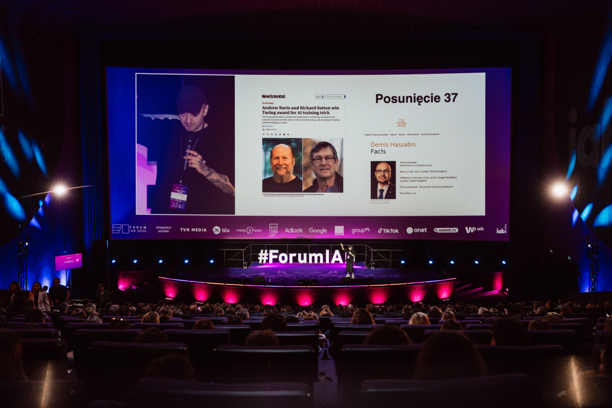 Prelegent prezentuje na scenie podczas #ForumIA, z dużym ekranem wyświetlającym slajdy o sztucznej inteligencji i znanych postaciach. Publiczność siedzi w ciemnym, nowoczesnym audytorium z kolorowymi światłami.