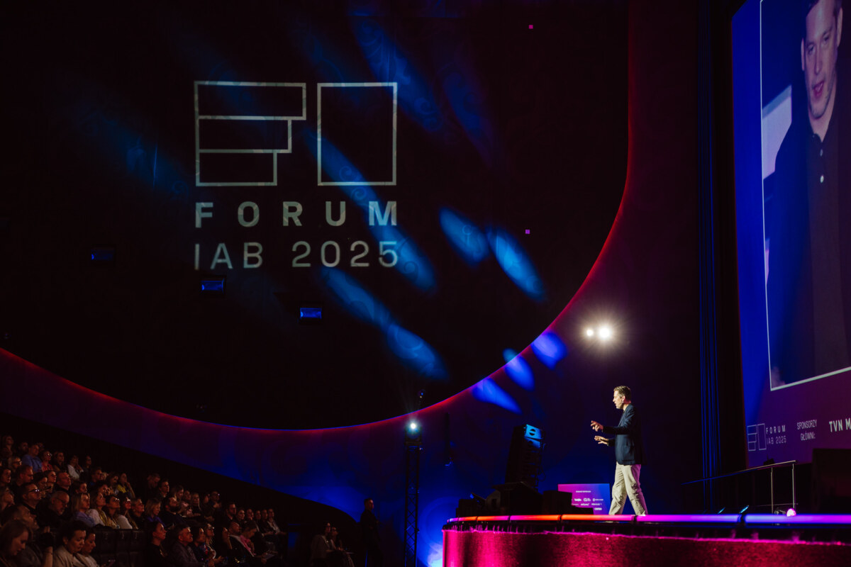 Prelegent prezentuje na scenie podczas dużej konferencji z napisem "FORUM IAB 2025" wyświetlanym na ścianie i publicznością siedzącą w ciemnym audytorium. Duży ekran pokazuje zbliżenie mówcy.