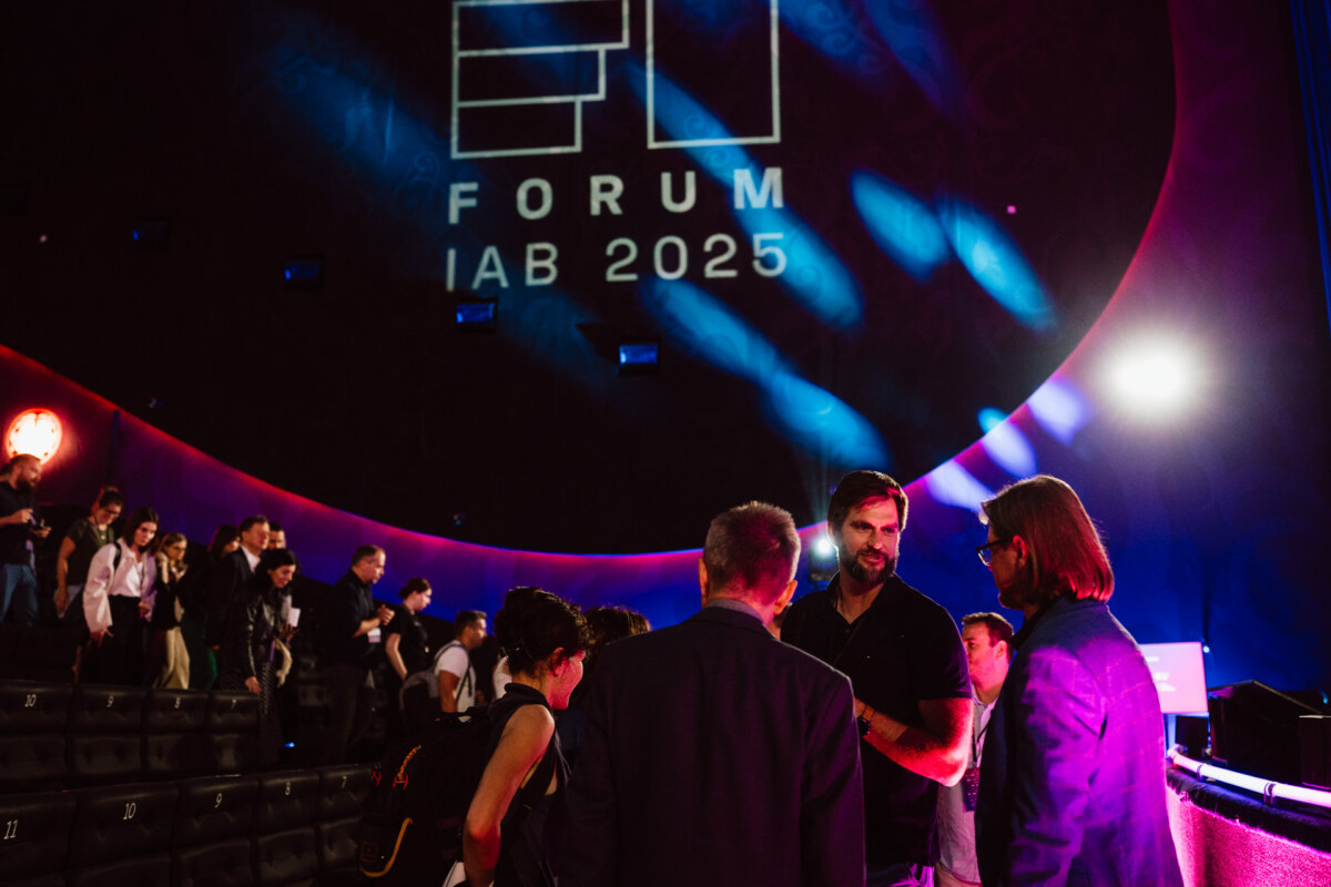 Tłum ludzi gromadzi się i rozmawia w słabo oświetlonym audytorium. "FORUM IAB 2025" jest wyświetlane dużymi literami na tylnej ścianie nad ich głowami.