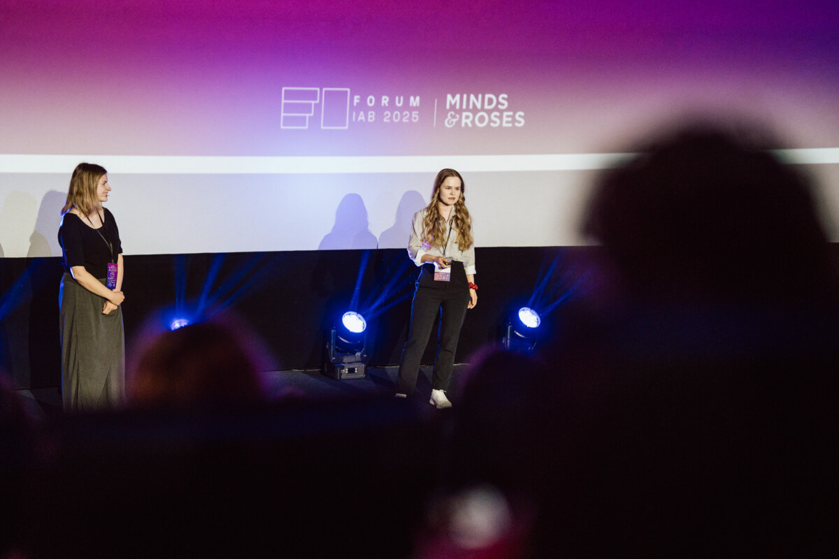 Dwie kobiety stoją na scenie przy fioletowym oświetleniu podczas wydarzenia "Forum LAB 2025 Minds & Roses", z sylwetkami publiczności widocznymi na pierwszym planie.