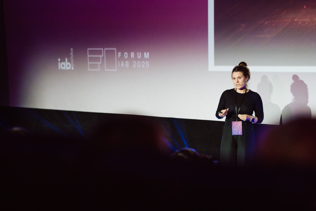 Kobieta stoi na scenie, prowadząc prezentację na Forum IAB 2025, przemawiając przed wyświetlanym ekranem z logo wydarzenia i fioletowym tłem.