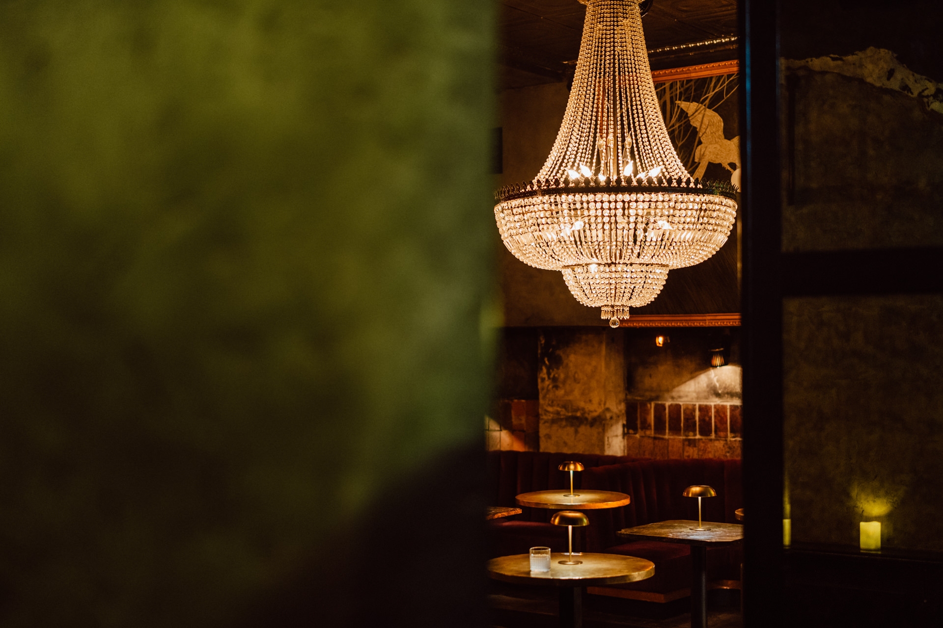 Fotograf na impreze firmowa weles bar warszawa2 Kryształowy żyrandol wisi nad pustymi okrągłymi stolikami w słabo oświetlonej, eleganckiej restauracji lub barze z meblami z ciemnego drewna i ciepłą, zachęcającą atmosferą.