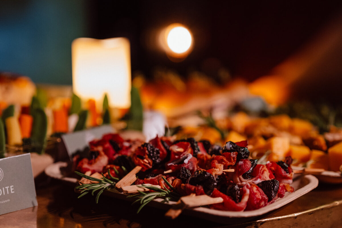 Fotograf na impreze firmowa weles bar warszawa6 1 Zbliżenie na elegancką przystawkę rozłożoną na stole, zawierającą szaszłyki z wędlinami i suszonymi owocami, warzywa, kostki sera i świecącą świecę w tle, tworzącą ciepłą, świąteczną atmosferę.