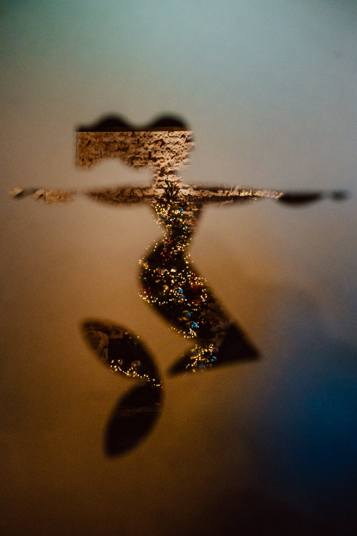 Niewyraźne odbicie osoby z wyciągniętymi ramionami, widoczne przez zamgloną powierzchnię z plamą czystego obszaru ozdobionego małymi kolorowymi światłami lub ornamentami.