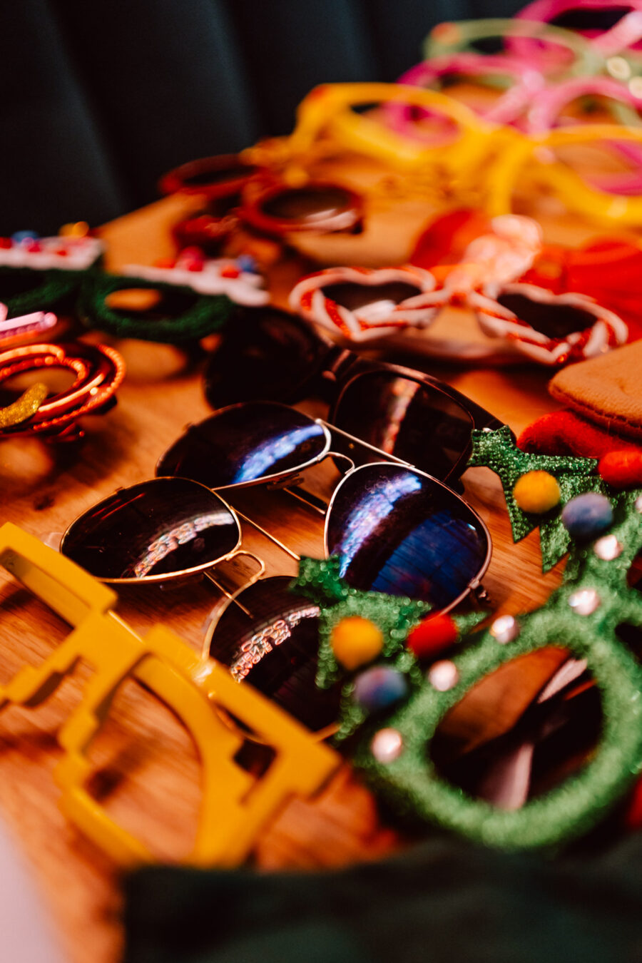 wigilia firmowa spoldzielnia koneser fotograf na impreze 010 Różnorodne kolorowe okulary przeciwsłoneczne i nowatorskie okulary, w tym aviator i w kształcie choinki, są rozłożone na drewnianej powierzchni.
